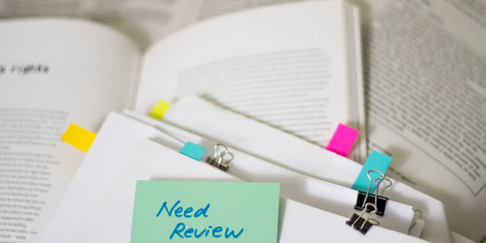 Image of a post-it note with the words 'Need Review' written on it, stuck on top of a pile of documents, illustrating the concept of altering the articles of association for a charitable limited company