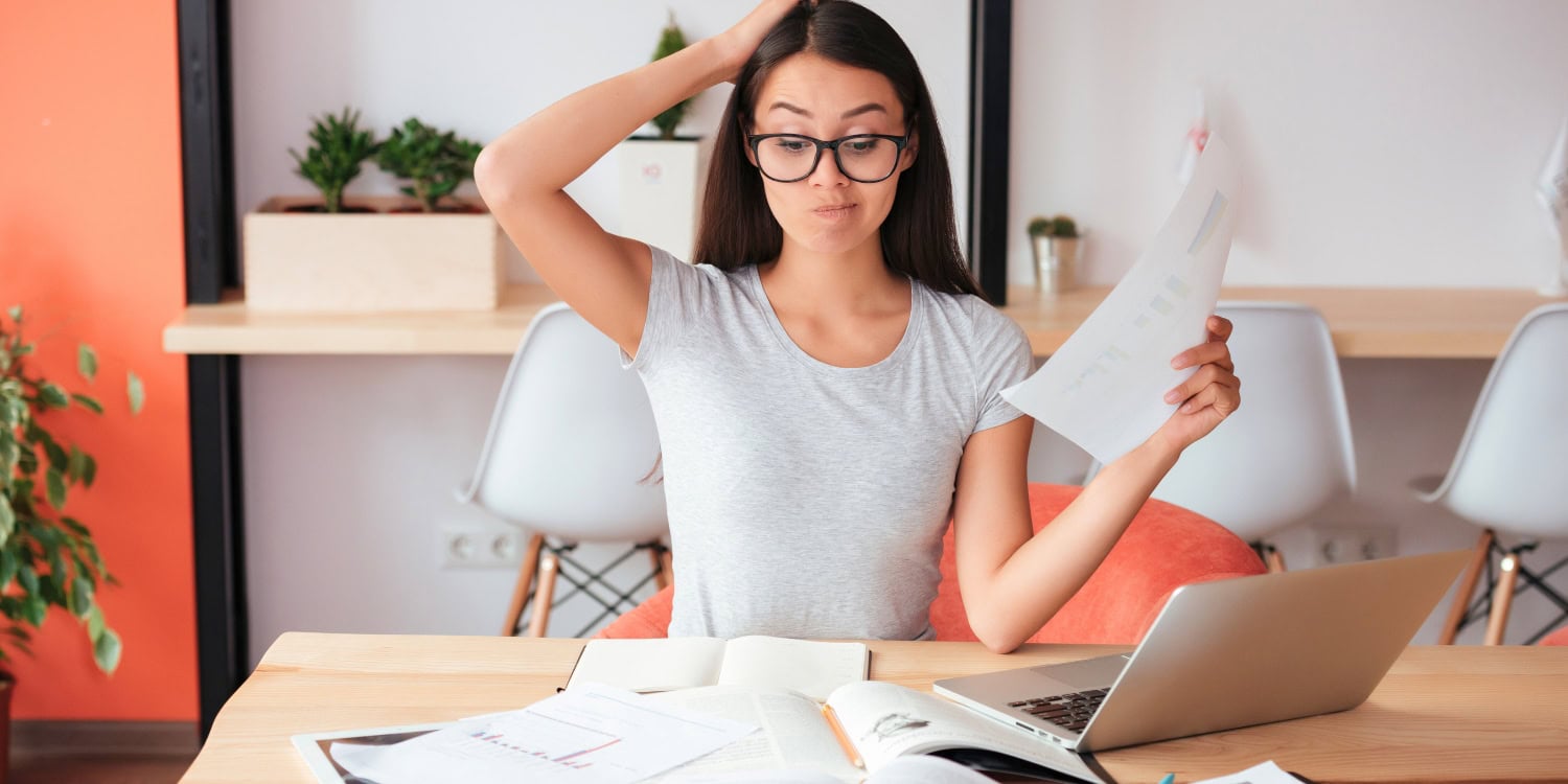 Woman holding paperwork and scratching her head while working at a laptop, representing the challenge of keeping records for a limited company.