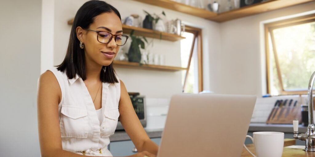 Sole trader working on a laptop in a bright kitchen, thoughtfully considering whether to transition to forming a limited company