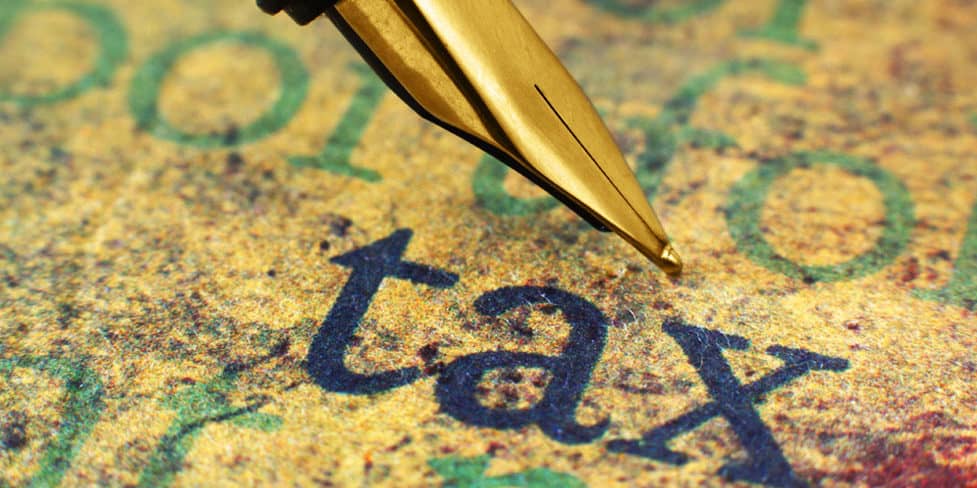 Image of the tip of a fountain pen above a piece of paper with the word 'tax' typed on it.