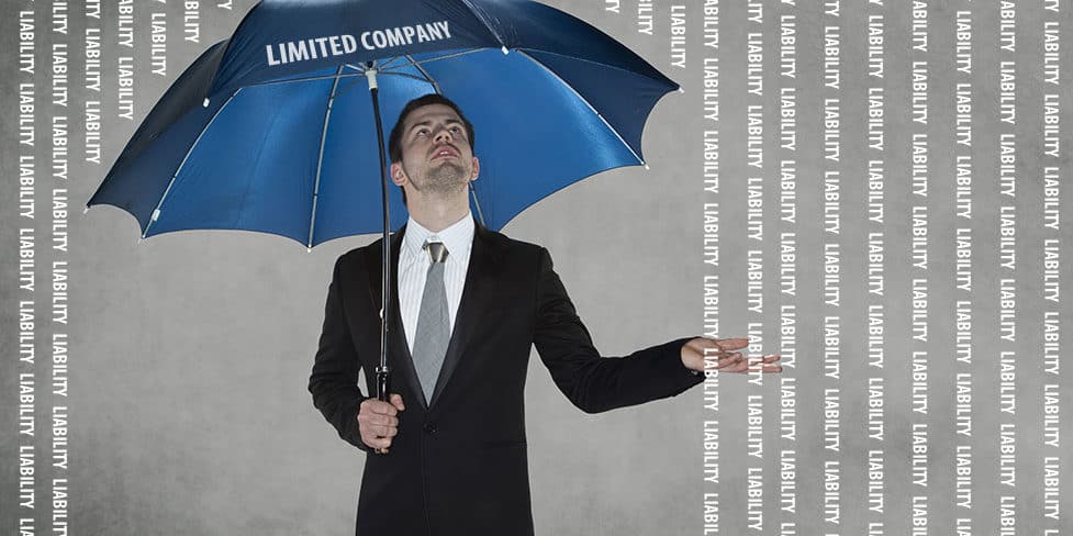 An image of a man in a suit, holding a blue umbrella above his head as the word 'liability' rains down on him. This is used to illustrate that liability for business debts is an important consideration when deciding whether to operate as a sole trader or limited company.