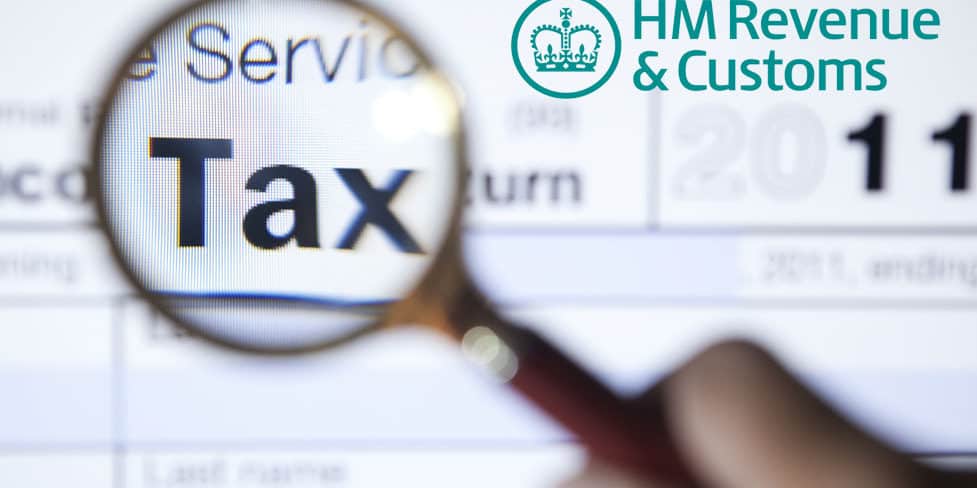 Magnifying glass held over an HMRC tax return form, highlighting the word 'Tax'.