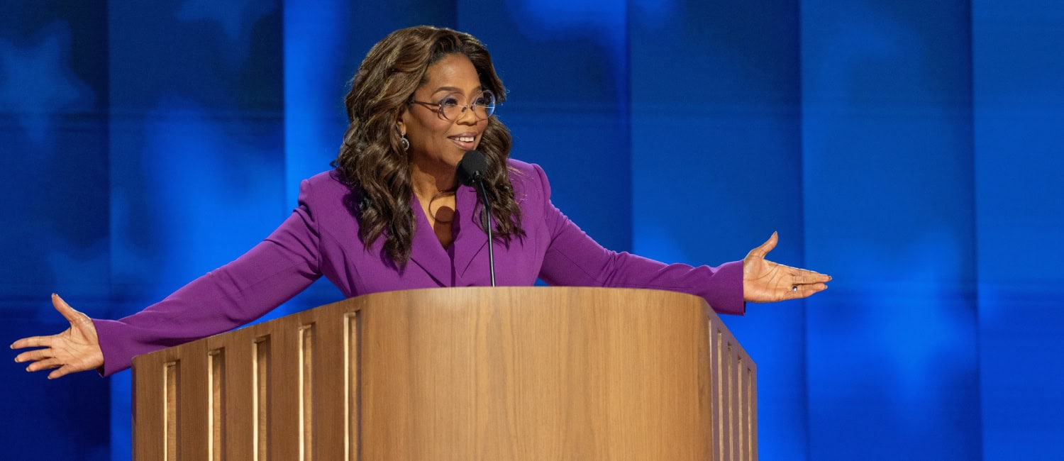 Опра Уинфри страстно говорит на сцене, жестикулирует руками на фоне синего экрана.