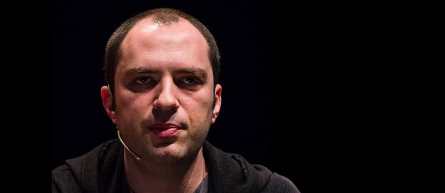 Крупный план Яна Кума с короткой стрижкой и гарнитурой на фоне темного фона.