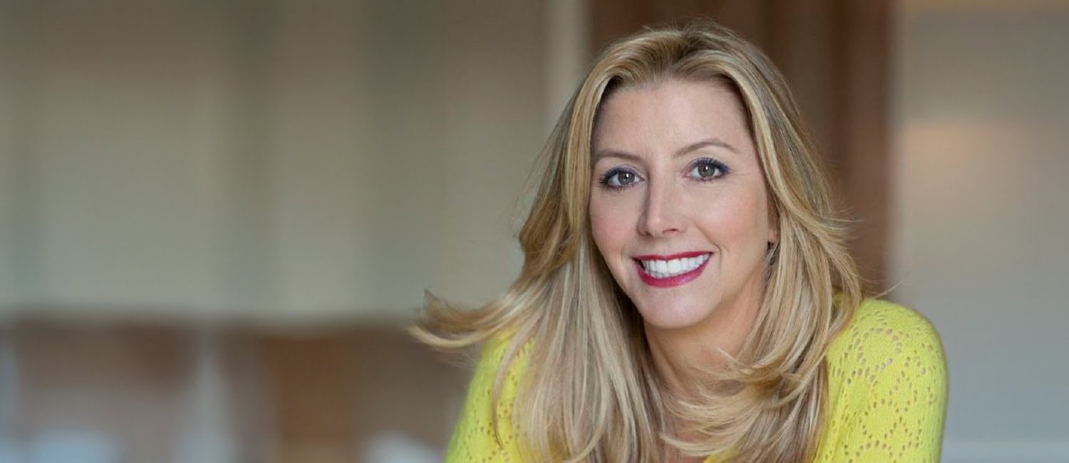 Сара Блейкли в ярко-желтой рубашке с длинными светлыми волосами на мягко размытом фоне.