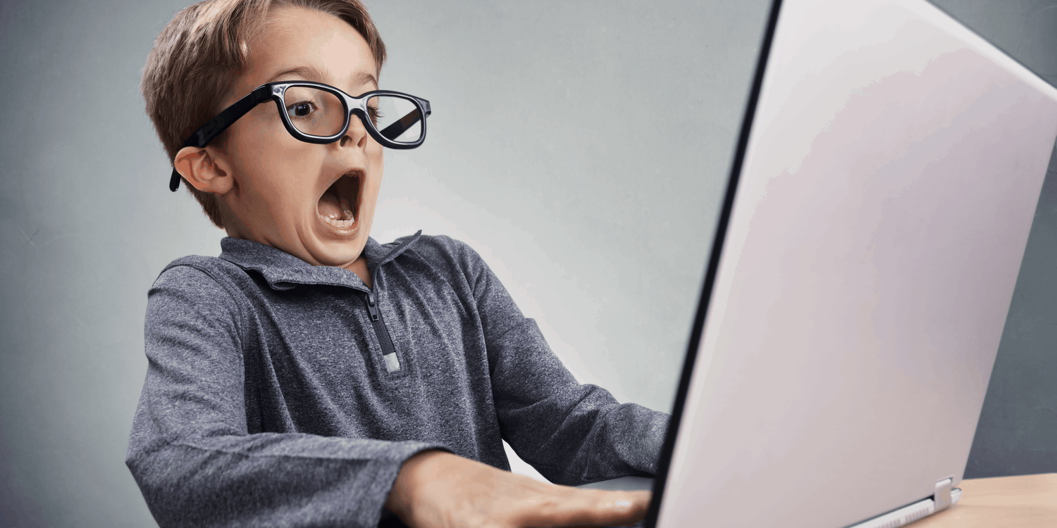 Schoolboy with large spectacles looking at laptop with shocked and surprised expression.