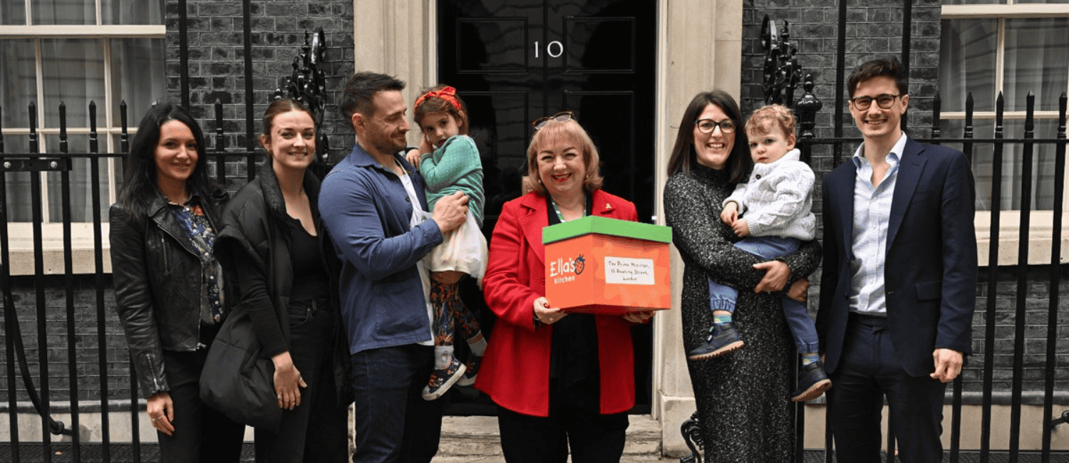 A group gathers outside Number 10 Downing Street with a colourful box labelled "Ella's Kitchen," smiling for the camera.