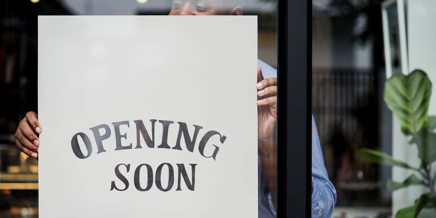 Shop owner holding 'opening soon' sign behind clear door