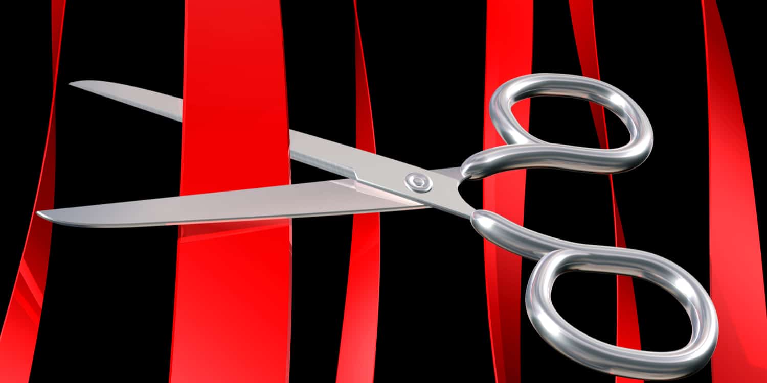 Pair of silver scissors cutting through red tape.