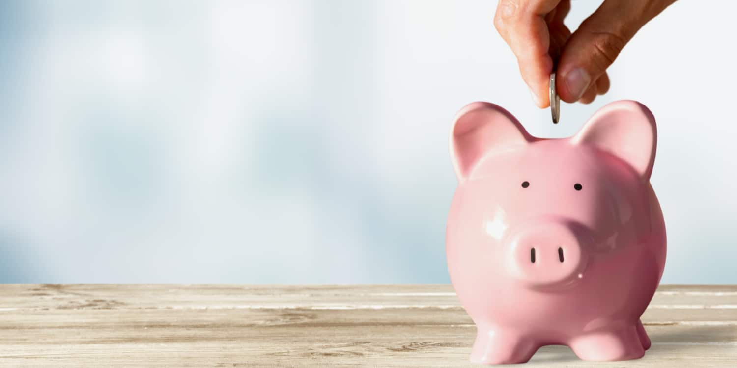 Pink piggy bank on wooden table with hand placing coin in it