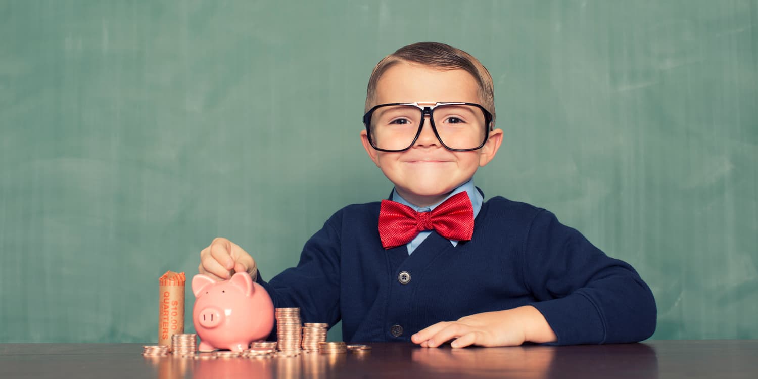 Little boy with glasses and red bowtie sat with a piggy bank and coins