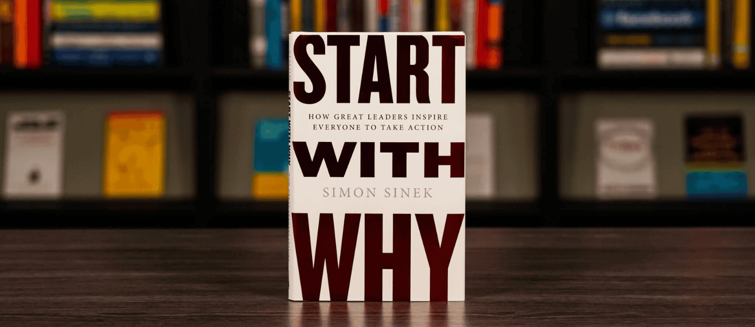 Cover of "Start With Why" by Simon Sinek, with bold text on a minimalistic design. The background features a blurry bookshelf with various books.