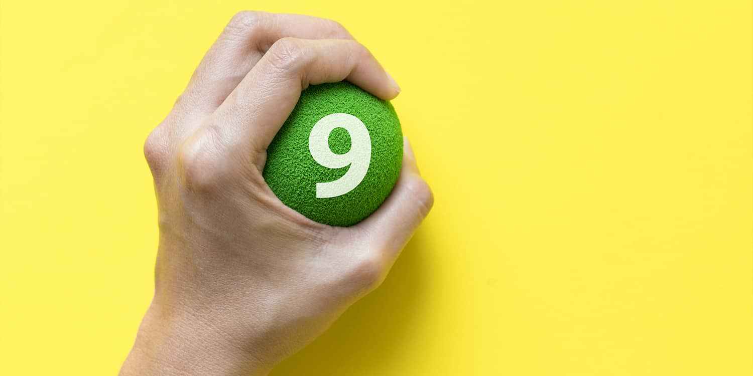 Hand grasping green stress ball with '9' written on it, on yellow background