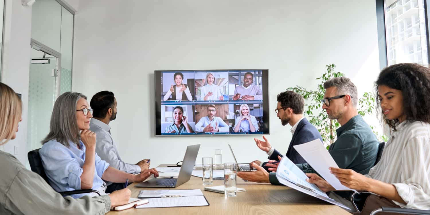 Group of company shareholders attending a general meeting - sitting around a meeting table and others attending via conference call.