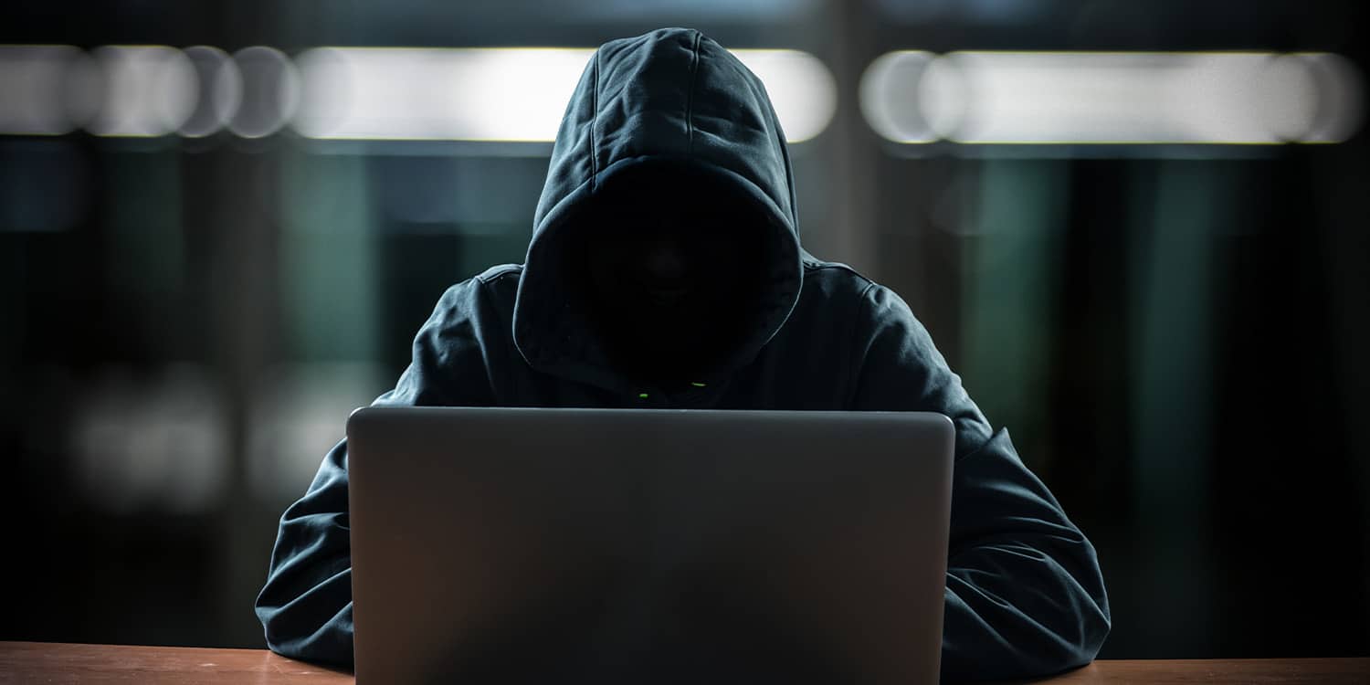 Photo of person whose face is obscured by a hoodie sat at a laptop
