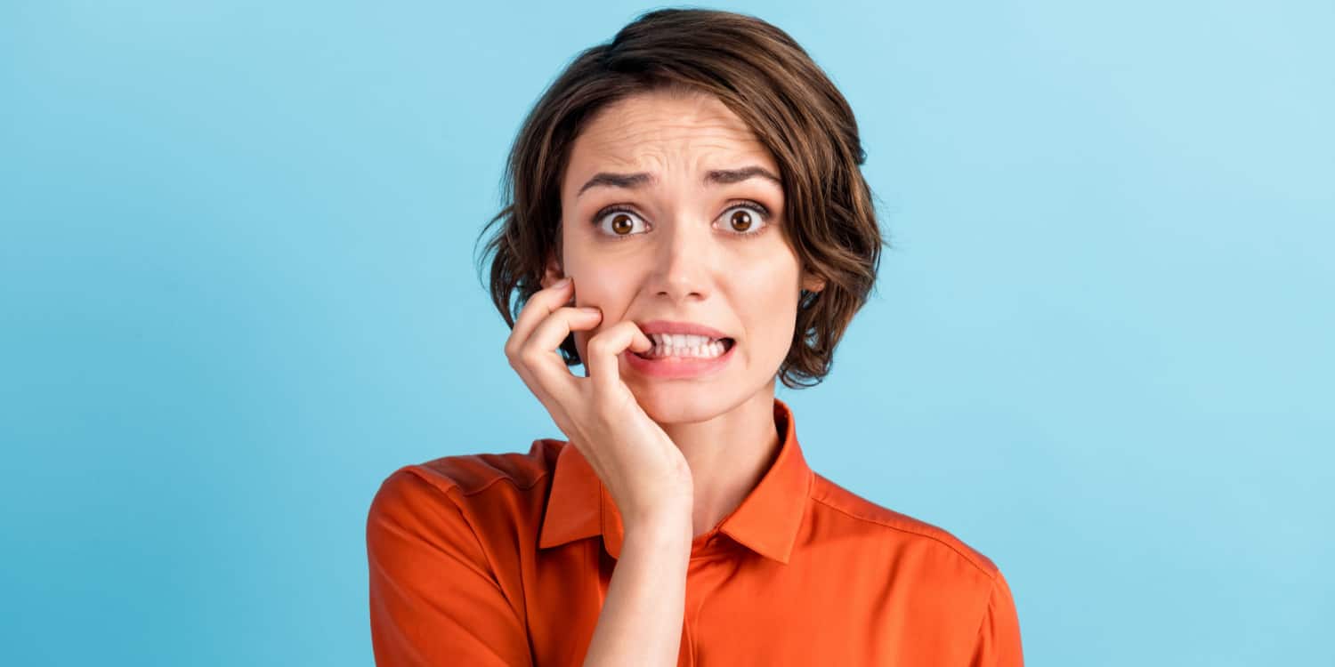 Closeup photo of a lady with a horrified facial expression after making a filing mistake, wearing an orange shirt against a blue background