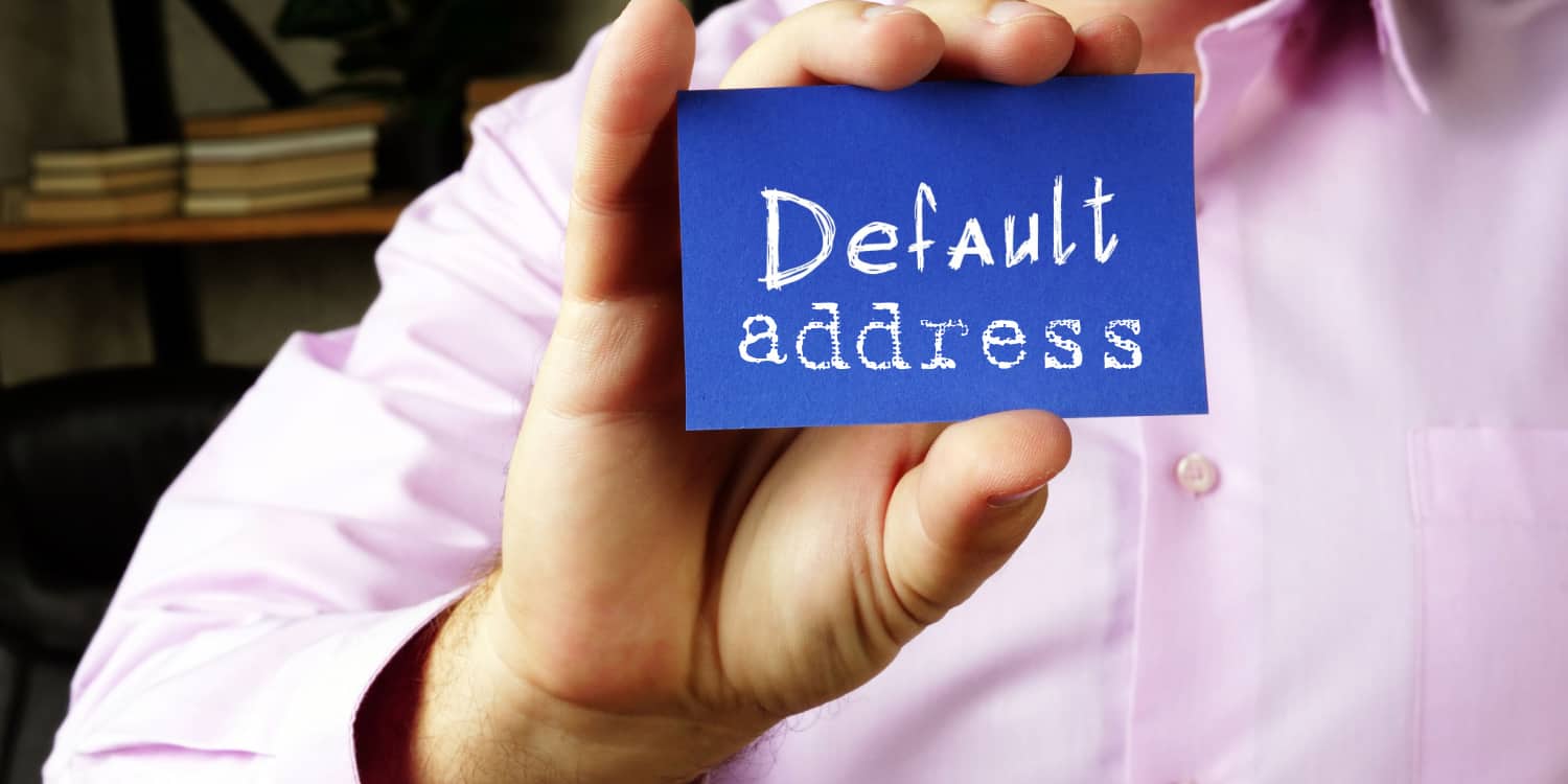 Businessman in pink short holding up small blue card with 'default address' written in white font.