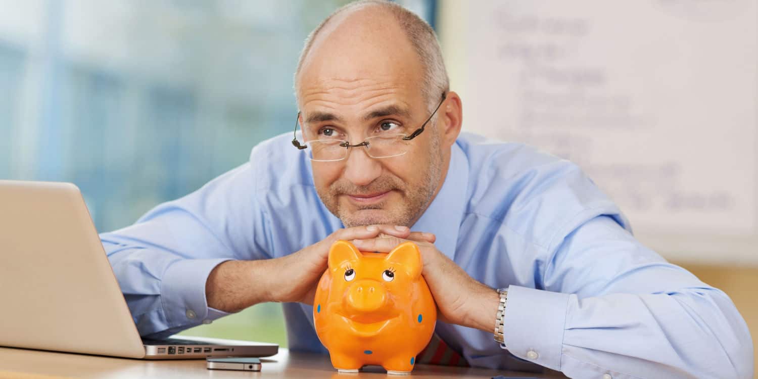 Thoughtful businessman sitting with hands on a piggy bank, thinking about his company director pension contributions.