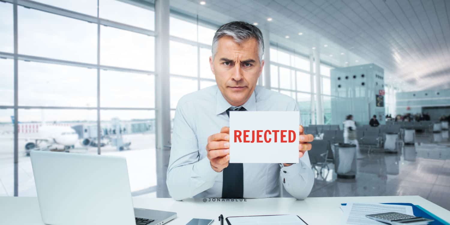 Frowning businessman at desk holding a REJECTED sign - illustrating the concept of a company formation rejection.