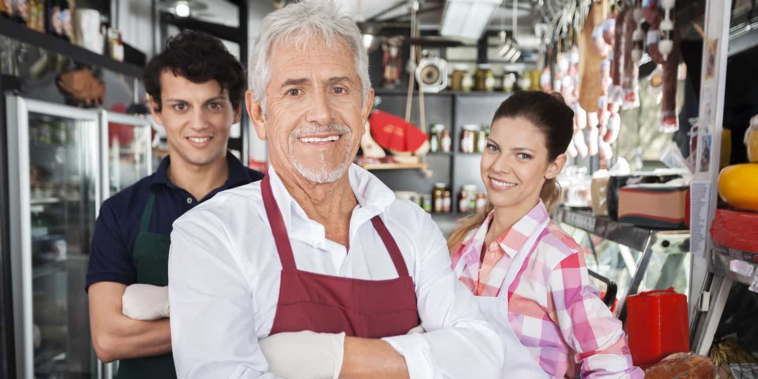 Portrait of father, son and daughter, standing smiling at the camera, in their cheese shop business.