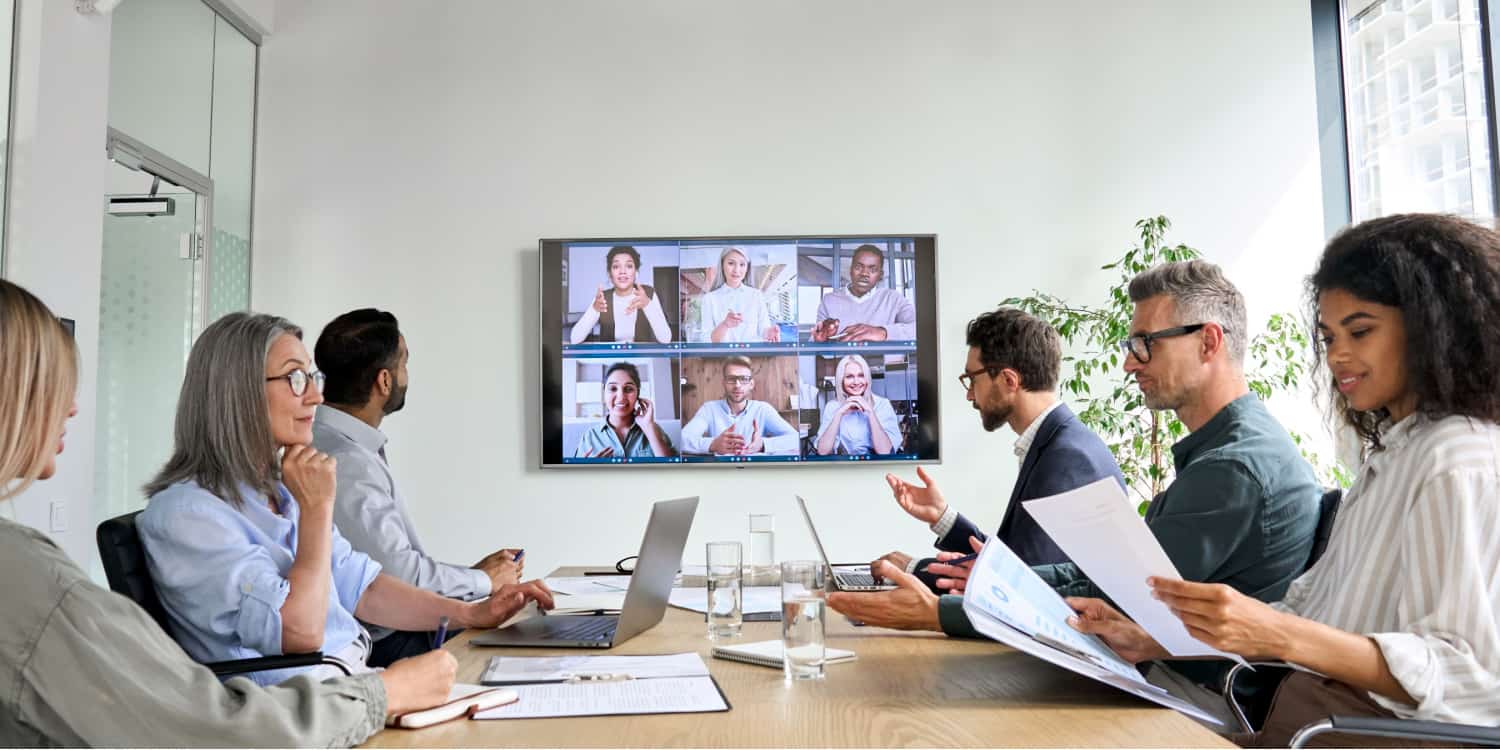 Company directors holding a board meeting in their conference room with other directors attending by video call and displayed on a wall mounted monitor screen.