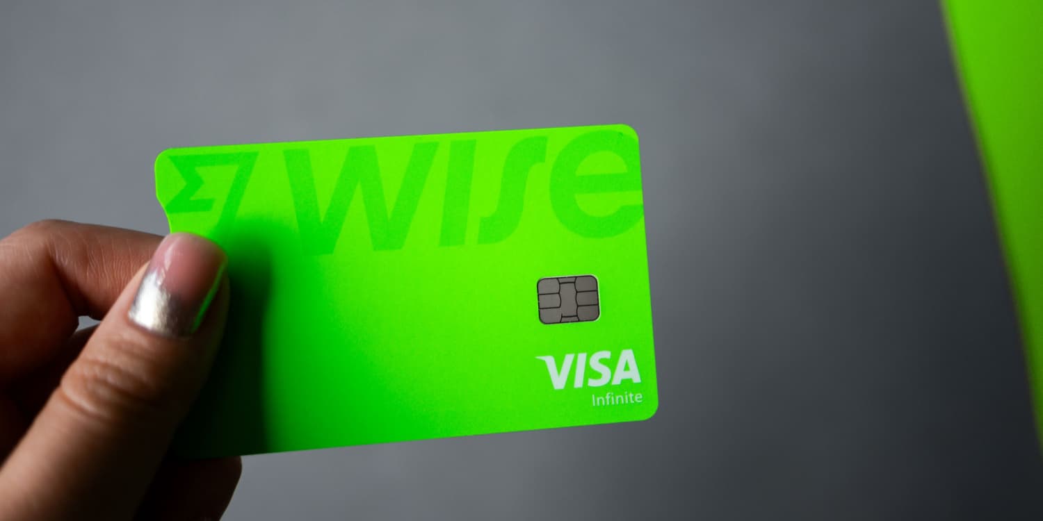 A female hand holding a Wise Business Account card against a grey background.