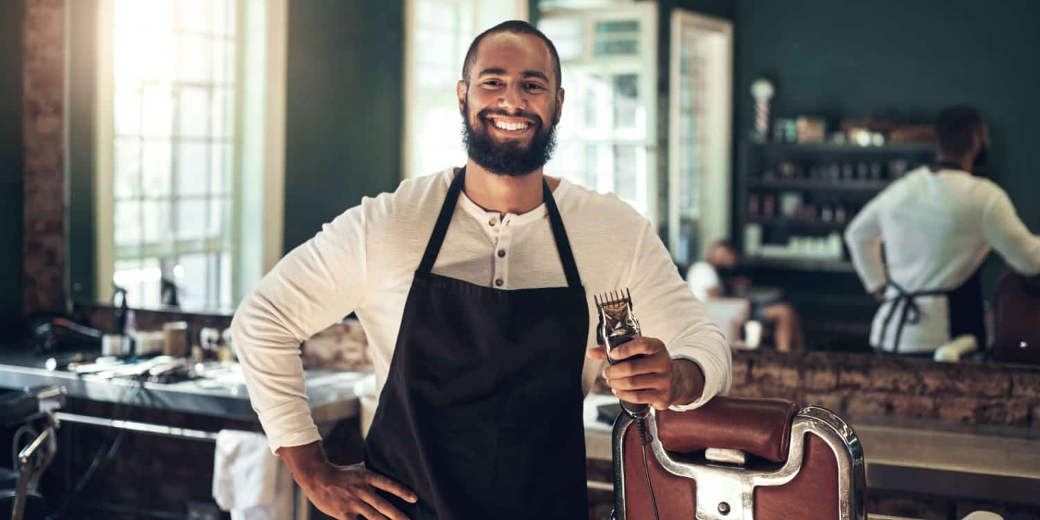 Portrait of a smiling barber shop owner, standing in his shop and holding hair clippers.