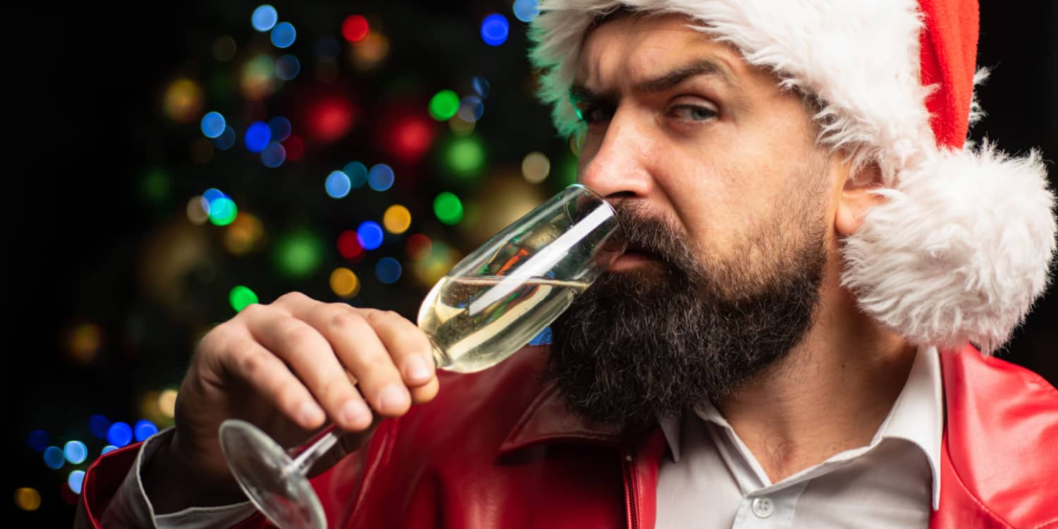 Business owner dressed as Santa Claus and drinking champagne at the office Christmas party.