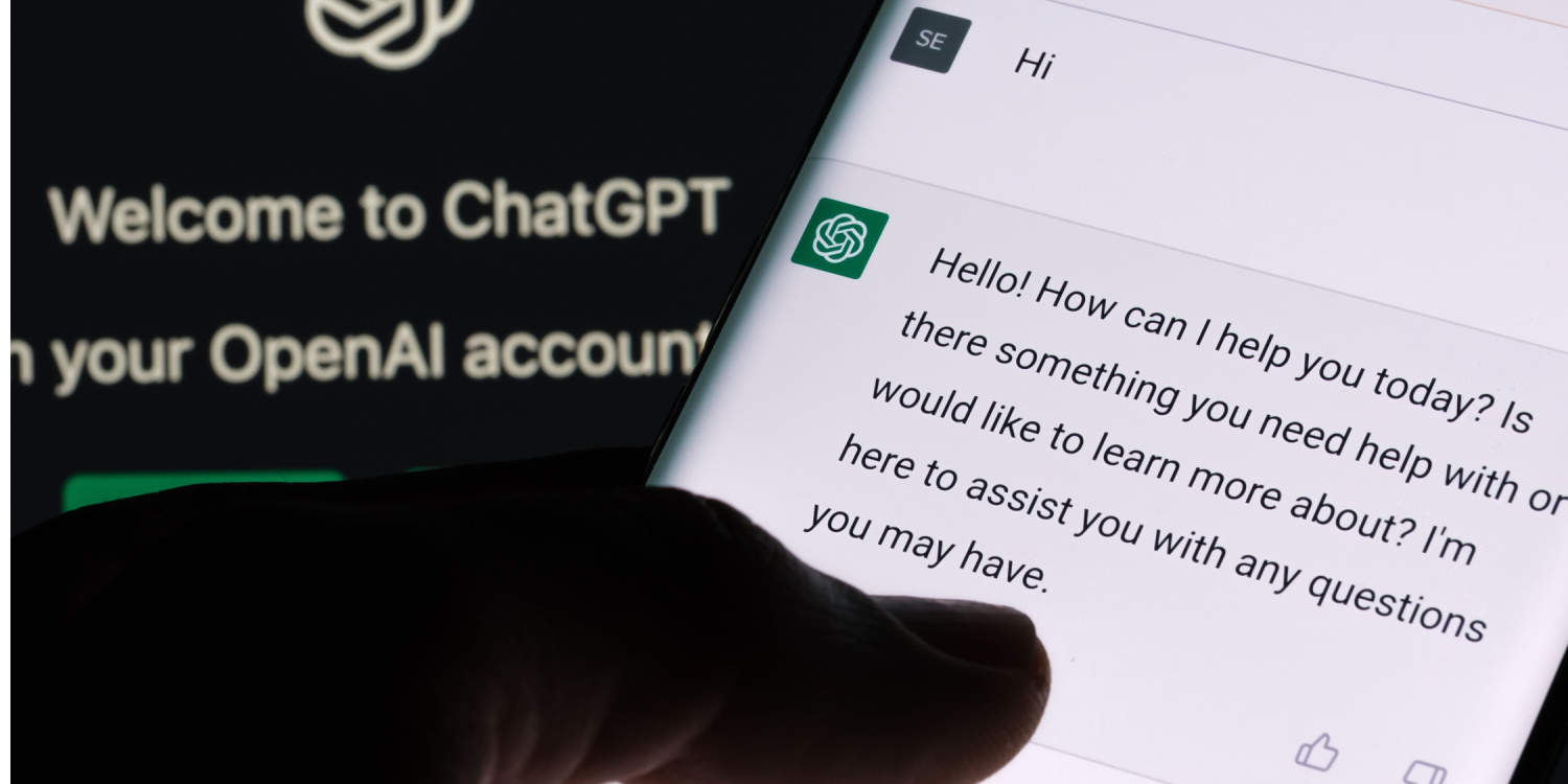 ChatGPT AI chat bot screen seen on smartphone with laptop screen in the background displaying ChatGPT login screen.