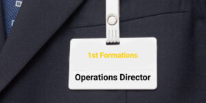 White name tag on a grey suit displaying the name of the company - 1st Formations, and the job title - Operations Director.