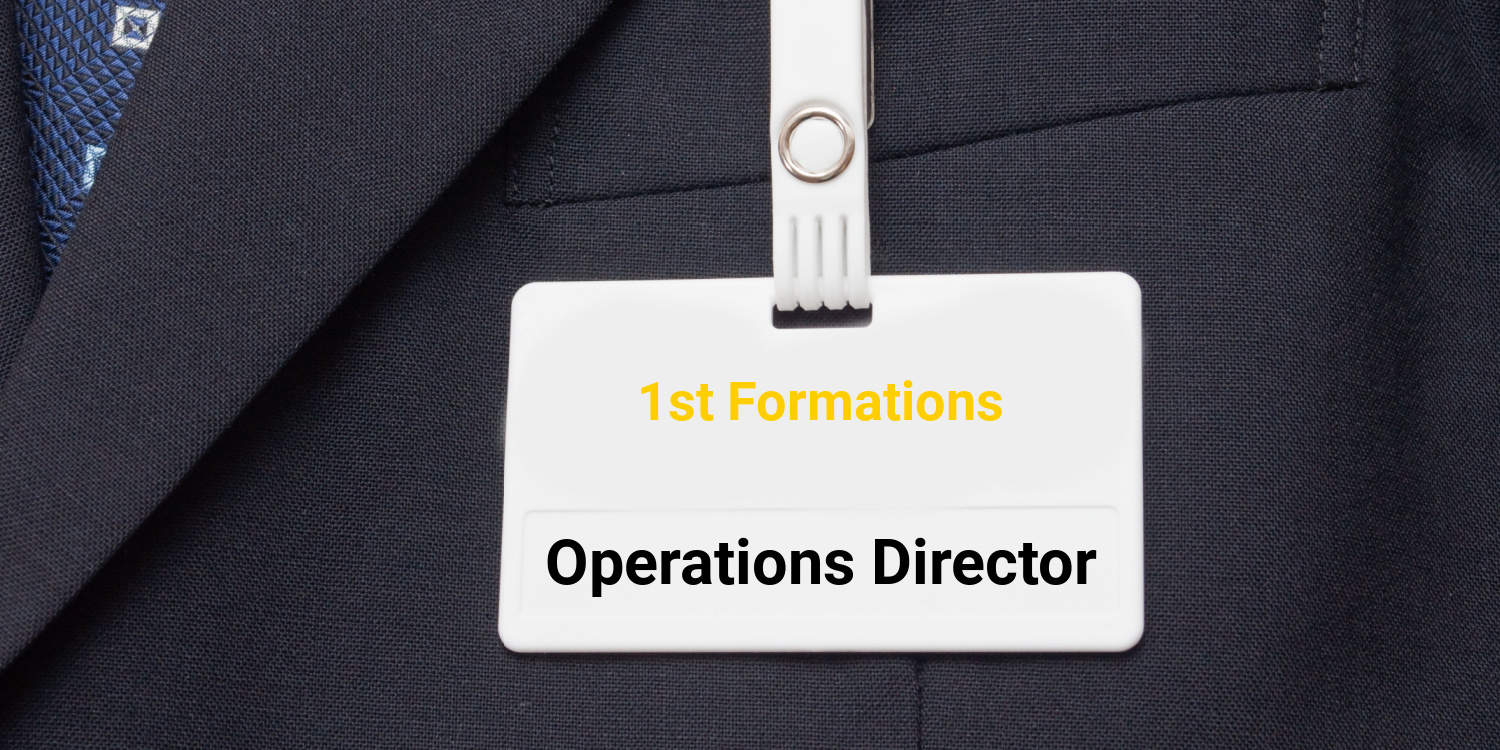 White name tag on a grey suit displaying the name of the company - 1st Formations, and the job title - Operations Director.