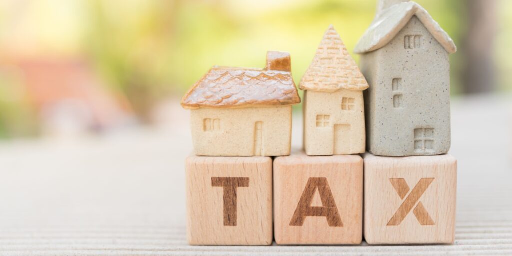 The word TAX is displayed on 3 wooden blocks with miniature homes sitting on top of the blocks.