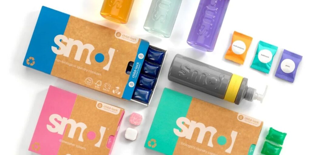 Colorful packaging of smol laundry capsules and dishwasher tablets, alongside plastic dispensers featuring eco-friendly designs.