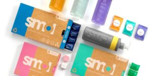 Colorful packaging of smol laundry capsules and dishwasher tablets, alongside plastic dispensers featuring eco-friendly designs.
