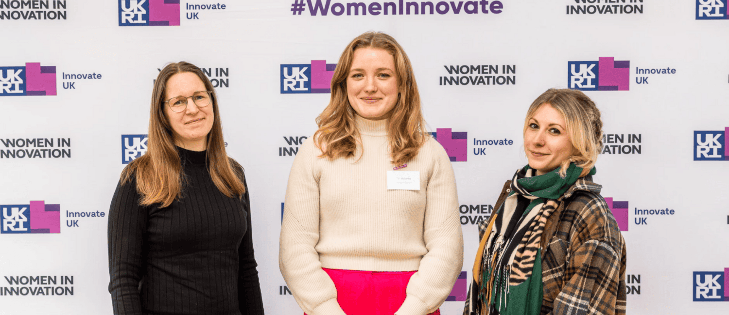Three women stand together in front of a backdrop featuring the "Women in Innovation" campaign and "Innovate UK" logos.