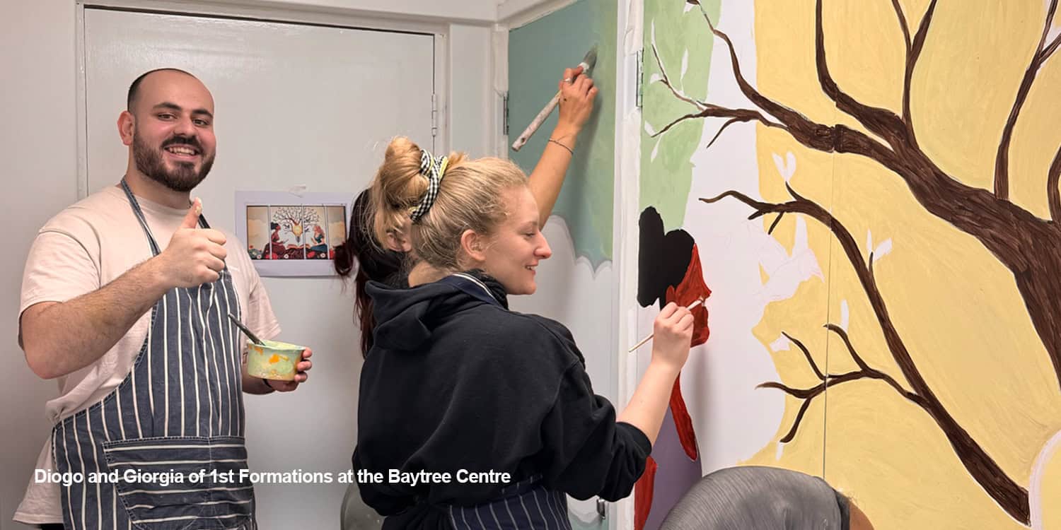 Employees painting a mural together indoors during corporate volunteering days at a community centre.