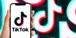 A hand holding a smartphone displaying the TikTok logo, with vibrant background patterns reflecting the app's iconic colours.