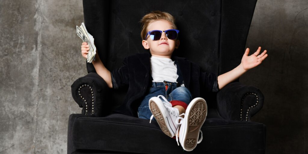 Happy young shareholder/director wearing sunglasses, sitting in a chair and celebrating success with a handful of money.