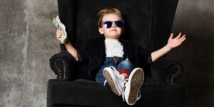 Happy young shareholder/director wearing sunglasses, sitting in a chair and celebrating success with a handful of money.