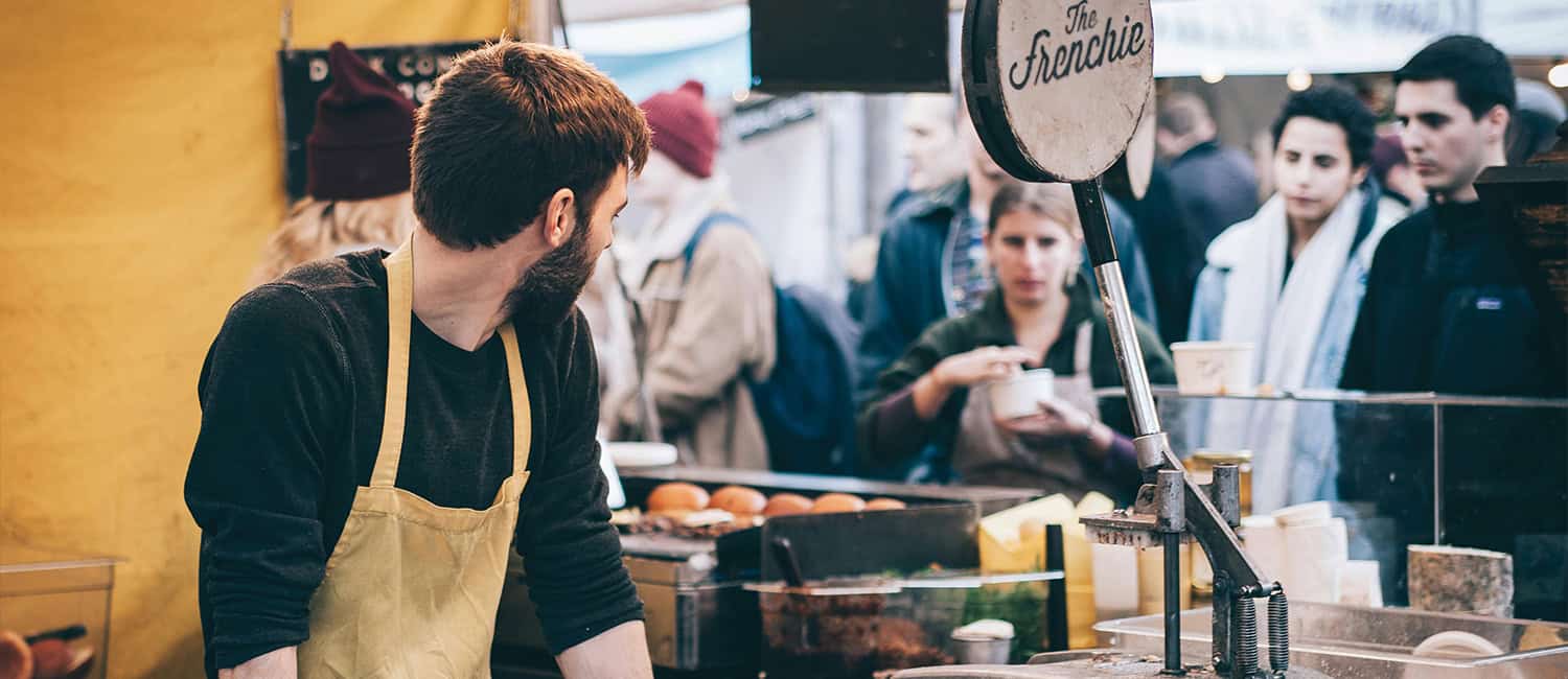 Market stall owner serving food to a queue of customers, capturing the hustle of small business life and the energy of running a business