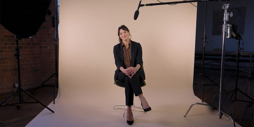 A young woman dressed in a suit is interviewed in a film studio about entrepreneurship