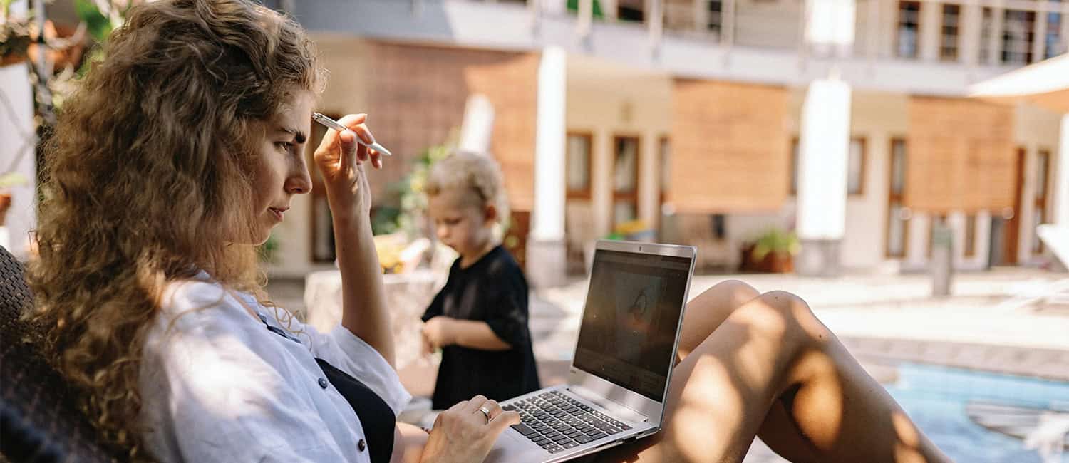 Woman using a laptop by the pool while holding a pen, researching digital tools, resources, and startup guidance