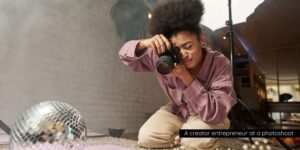 A creator entrepreneur crouches on the floor, capturing photos of a disco ball and other items with a camera, surrounded by soft lighting and props.