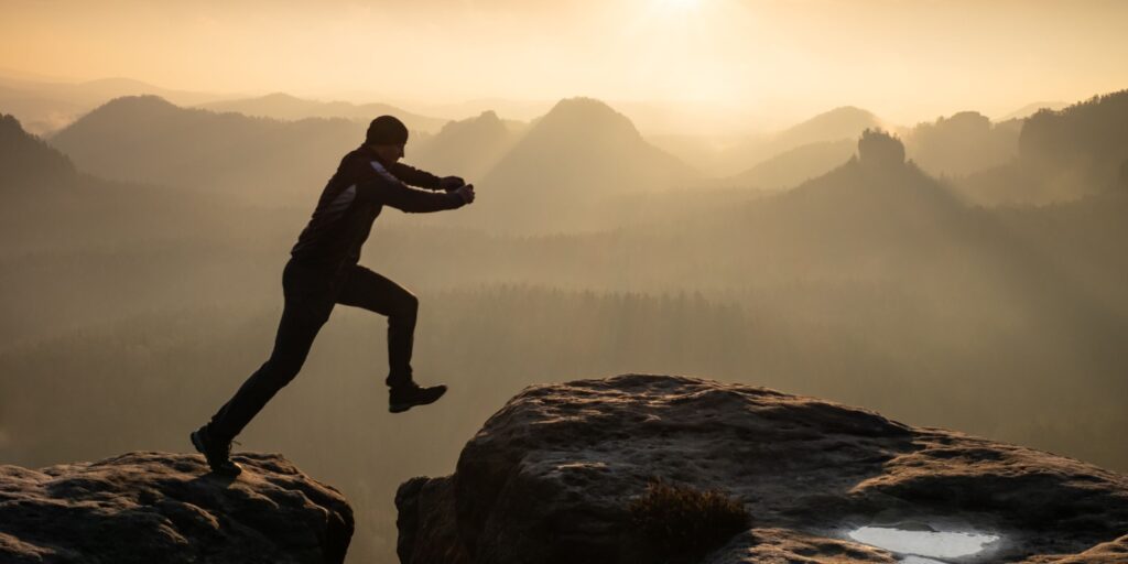 Person leaping between two cliffs at sunrise, symbolising courage and being ready to start a business with confidence and determination
