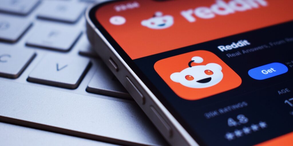Close-up of a smartphone displaying the Reddit app download page, placed on a laptop keyboard, representing the use of Reddit for digital marketing strategies