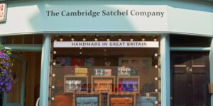 Shopfront of The Cambridge Satchel Company displaying a variety of handmade leather satchels and a sign reading 'Handmade in Great Britain'