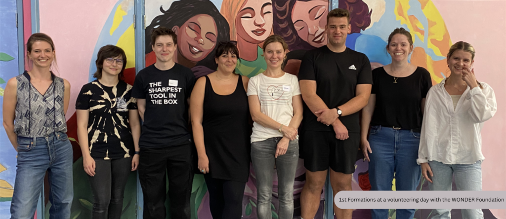 1st Formations staff standing together during a business volunteering day with the charity WONDER Foundation, in front of a colourful mural painted as part of the initiative