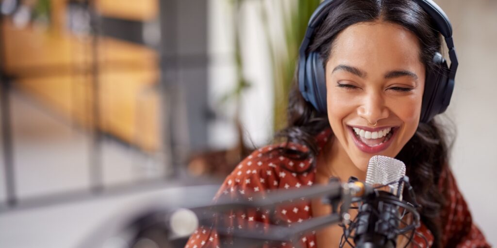 Cheerful young latin woman recording a podcast in a studio with large microphone and boom.