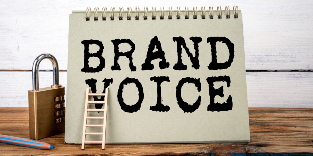 A green notepad with the words BRAND VOICE displayed in block capitals and black font - on a wooden table.