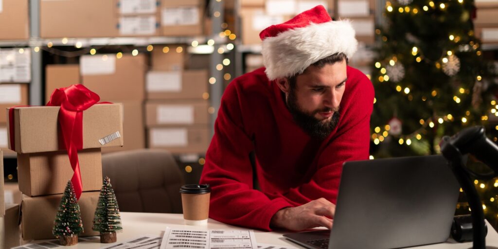 A man in a festive hat working on a laptop, preparing his business for Christmas